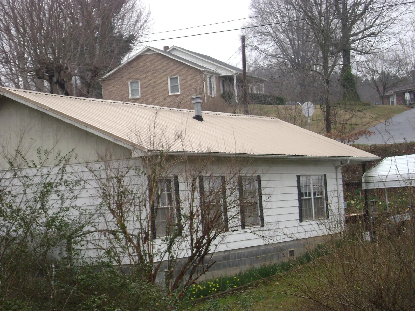 Tan metal roof on a white sided house set into a hillside — Commercial Roofing by Roofing Brothers in Cleveland